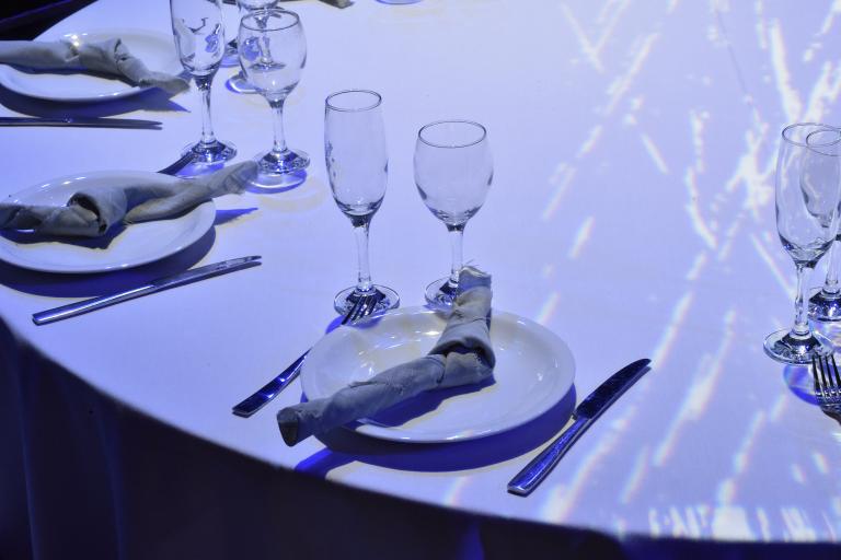 Dining table set with white tablecloth, plates and folded napkins, surrounded by wine and champagne glasses.