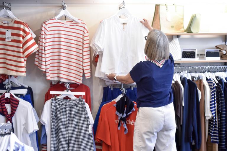 Person browsing clothing in a shop, reaching for a white top on a hanger.