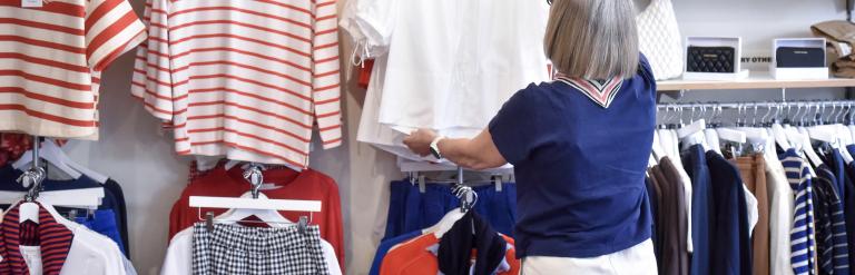 Person browsing clothing in a shop, reaching for a white top on a hanger.