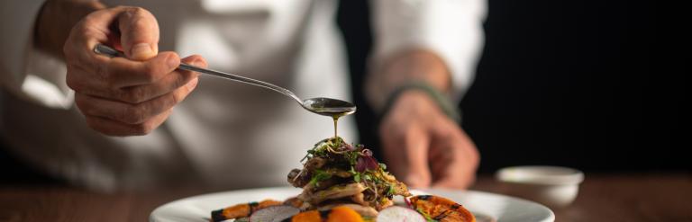 A male chef pouring sauce on meal